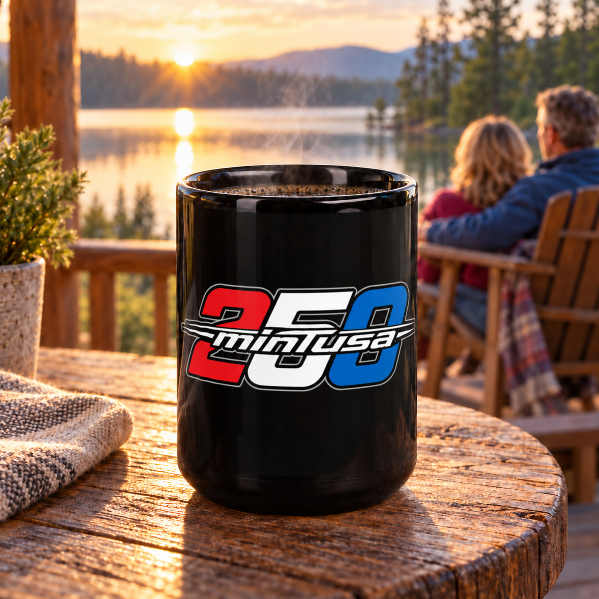 minTusa Celebrate 250 black 15-ounce mug on a lakeside cabin porch at sunrise