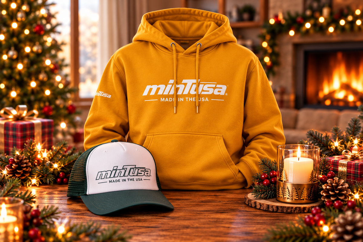 minTusa Signature Gift Set: a gold hoodie and a dark green and white foam trucker hat with the minTusa logo on a wooden table by a Christmas tree and fireplace